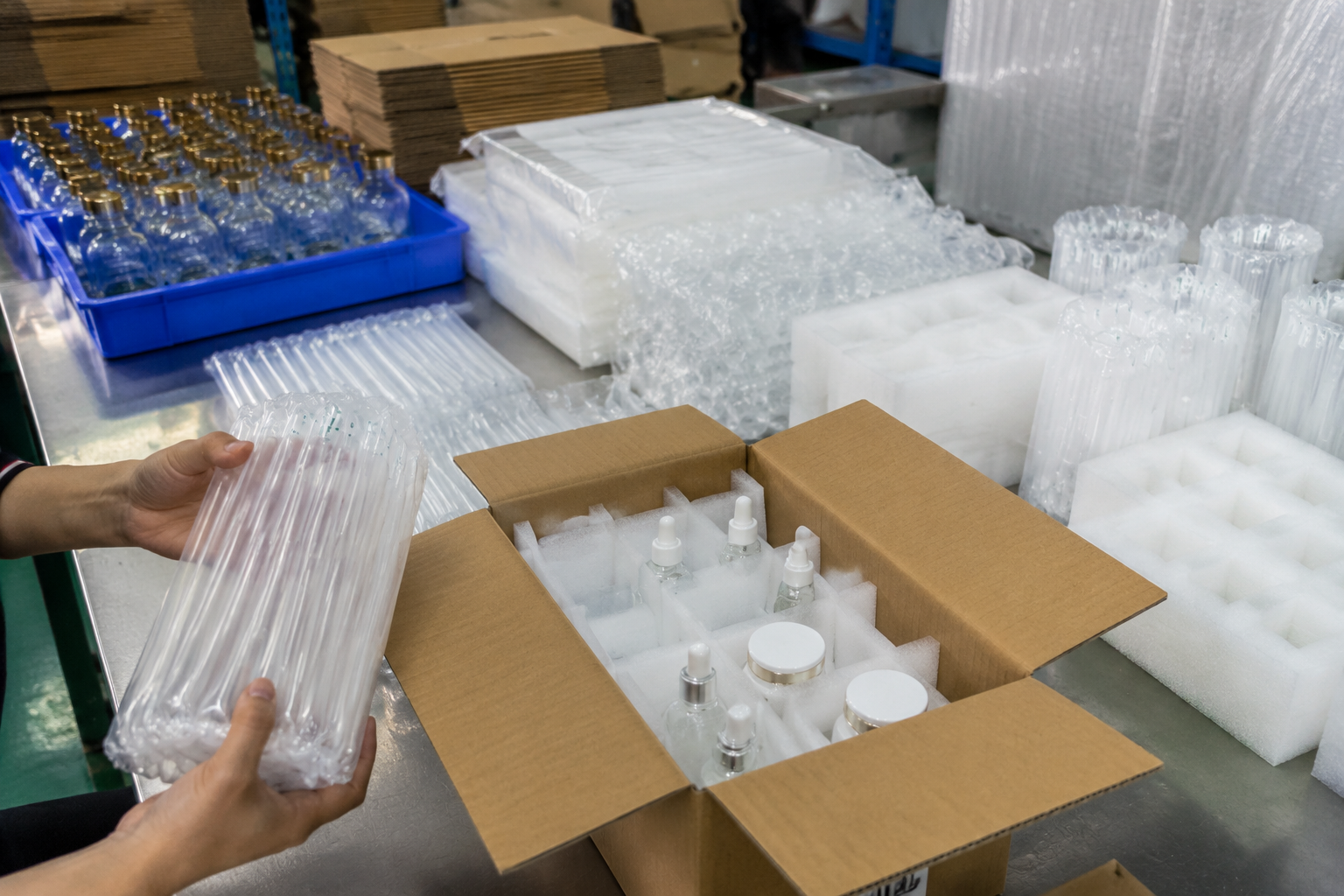 Glass bottles and cosmetic jars packed with air column bags, foam dividers, and corrugated carton protection on a factory packing table